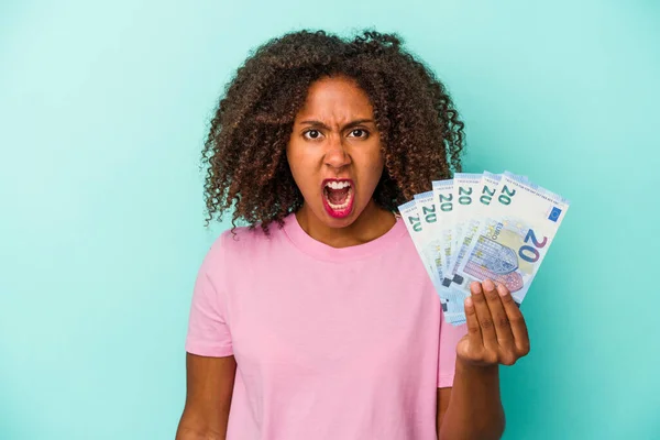 青の背景に孤立したユーロ紙幣を持っている若いアフリカ系アメリカ人女性は非常に怒って積極的に叫んで — ストック写真