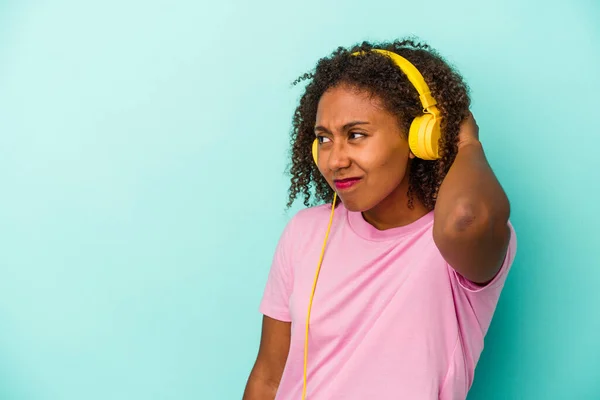 Young african american woman listening to music isolated on blue background touching back of head, thinking and making a choice.