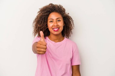 Beyaz arka planda izole edilmiş kıvırcık saçlı, gülümseyen ve baş parmağını kaldıran genç Afrikalı Amerikalı kadın.