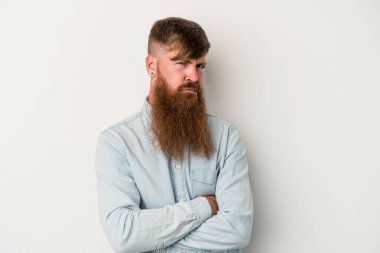 Beyaz arka planda uzun sakallı beyaz tenli genç beyaz adam alaycı bir ifadeyle kameraya bakıyor..