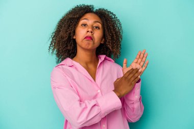 Mavi arka planda izole edilmiş kıvırcık saçlı, genç Afrikalı Amerikalı kadın enerjik ve rahat hissediyor, ellerini ovuşturuyor..