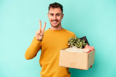 Genç beyaz adam mavi arka planda iki numarayı parmaklarıyla göstererek hareket ediyor..