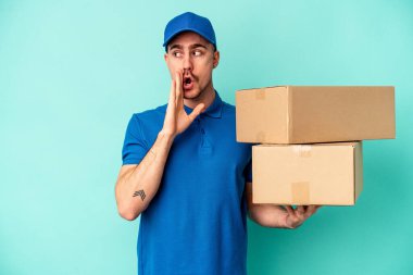 Genç teslimatçı beyaz adam mavi arka planda izole edilmiş gizli bir sıcak fren haberi veriyor ve yana bakıyor.