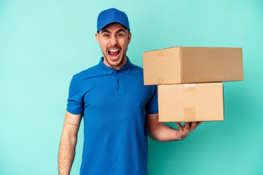 Genç teslimatçı beyaz adam mavi arka planda izole edilmiş çok kızgın ve agresif çığlık atıyor..