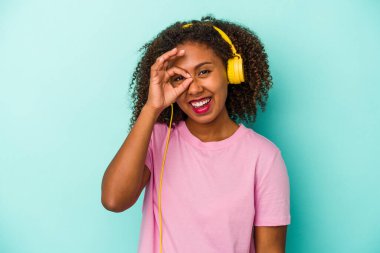Genç Afrikalı Amerikalı bir kadın mavi arka planda izole edilmiş müzik dinliyor..