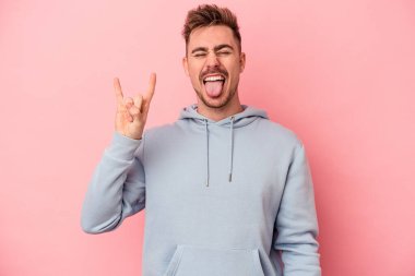 Pembe arka planda izole edilmiş genç beyaz adam parmaklarıyla taş hareketi gösteriyor.