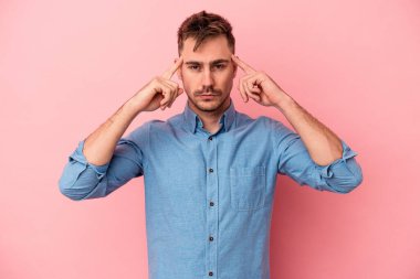 Pembe arka planda izole edilmiş genç beyaz adam bir göreve odaklanmış, parmaklarını işaret ediyor..