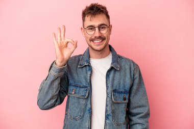 Pembe arka planda izole edilmiş genç beyaz adam neşeli ve kendinden emin, iyi bir hareket gösteriyor..