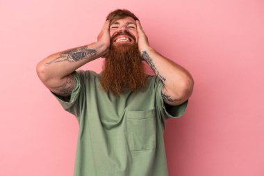 Pembe arka planda uzun sakallı, beyaz, genç bir adam ellerini başının üstünde tutarak gülüyor. Mutluluk kavramı.