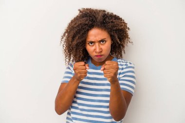 Beyaz arka planda izole edilmiş kıvırcık saçlı genç Afro-Amerikalı kadın kameraya yumruk gösteriyor, agresif yüz ifadesi var..