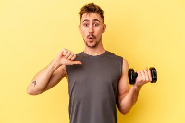 Sarı arka planda izole edilmiş bir halter tutan genç sporcu gururlu ve kendinden emin hissediyor, örnek olarak..
