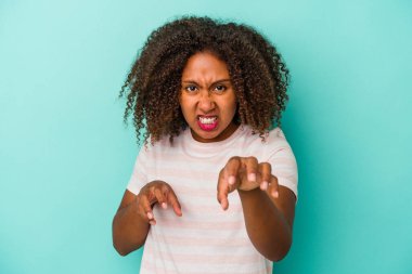 Mavi arka planda izole edilmiş kıvırcık saçlı, genç Afrikalı Amerikalı kadın pençelerini bir kediyi taklit ederken gösteriyor, agresif bir hareket..