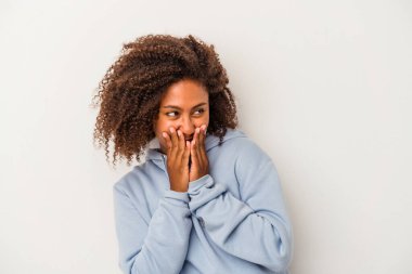 Beyaz arka planda yalıtılmış kıvırcık saçlı, genç Afro-Amerikalı bir kadın bir şeye gülüyor, elleriyle ağzını kapatıyor..