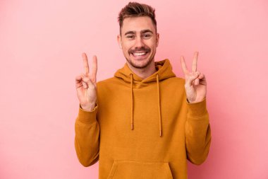 Pembe arka planda izole edilmiş genç beyaz adam zafer işareti gösteriyor ve gülümsüyor..