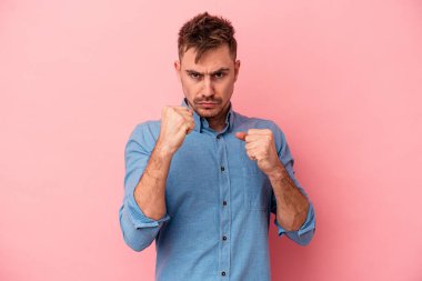 Pembe arka planda izole edilmiş genç beyaz adam yumruğunu kameraya gösteriyor, agresif yüz ifadesi var..