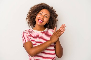 Beyaz arka planda yalıtılmış kıvırcık saçlı, enerjik ve rahat hisseden ellerini ovuşturan, kendine güvenen Afro-Amerikalı genç bir kadın..