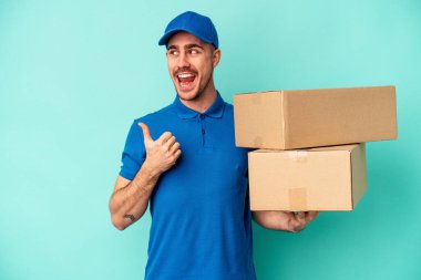 Genç teslimatçı beyaz adam mavi arka plan noktalarında izole edilmiş başparmak uzakta, gülüyor ve kaygısız.