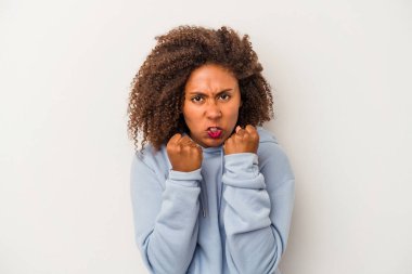 Beyaz arka planda izole edilmiş kıvırcık saçlı genç Afro-Amerikalı kadın kameraya yumruk gösteriyor, agresif yüz ifadesi var..