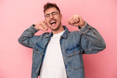 Pembe arka planda soyutlanmış genç beyaz adam özel bir günü kutluyor, atlıyor ve enerjiyle kollarını kaldırıyor..