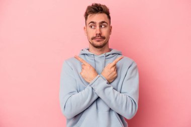 Pembe arka plan noktalarında izole edilmiş genç beyaz adam iki seçenek arasında seçim yapmaya çalışıyor..
