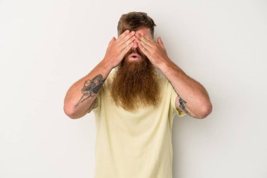 Beyaz arka planda uzun sakallı beyaz tenli genç beyaz adam elleriyle gözlerini kapatmaktan korkuyor..