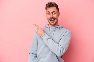 Pembe arka planda soyutlanmış genç beyaz bir adam gülümsüyor, neşeli ve keyifli görünüyor..