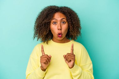 Mavi arka planda yalıtılmış kıvırcık saçlı, ağzı açık genç Afro-Amerikalı kadın..