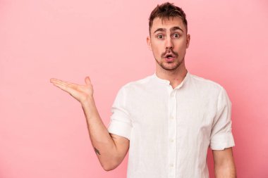 Pembe arka planda izole edilmiş genç beyaz adam, avuç içi fotokopi alanını elinde tutmaktan etkilenmiş..