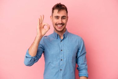 Pembe arka planda izole edilmiş genç beyaz adam neşeli ve kendinden emin, iyi bir hareket gösteriyor..