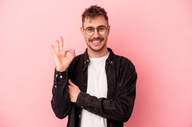 Pembe arka planda izole edilmiş genç beyaz bir adam bir göz kırptı ve elleriyle iyi bir jest yaptı..