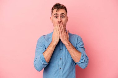 Pembe arka planda izole edilmiş genç beyaz adam elleriyle ağzını kapatırken şok oldu..