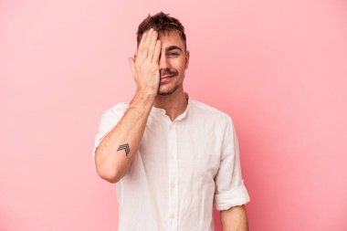 Pembe arka planda izole edilmiş genç beyaz adam yüzünün yarısını palmiye ile örterek eğleniyor..