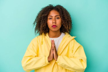 Mavi arka planda izole edilmiş kıvırcık saçlı genç Afrikalı Amerikalı kadın dua ediyor, kendini adamış, kutsal ilhamı arayan dindar biri..