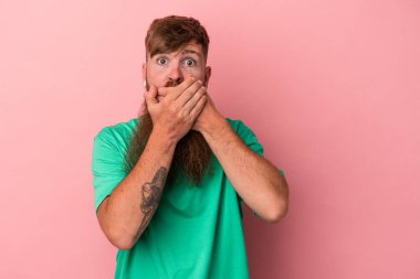 Uzun sakallı, beyaz, genç bir adam pembe arka planda izole edilmiş, ağzı kapalı ve elleri endişeli görünüyor..