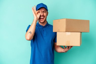 Genç teslimatçı beyaz adam mavi arka planda izole edildi. Heyecanlı görünüyor..