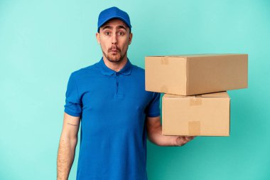 Mavi arka planda izole edilmiş genç bir beyaz adam omuzlarını silker ve gözleri açık kalır..