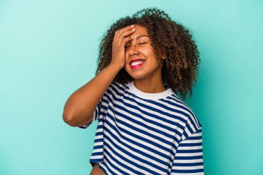 Mavi arka planda yalıtılmış kıvırcık saçlı, neşeli, kaygısız, doğal duyguları olan genç Afrikalı Amerikalı kadın..