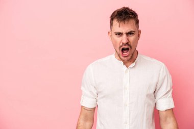 Pembe arka planda izole edilmiş genç beyaz adam çok kızgın, öfkeli, hayal kırıklığına uğramış diye bağırıyor..