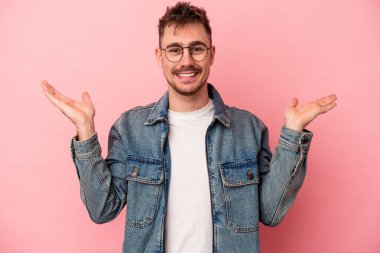 Pembe arka planda izole edilmiş genç beyaz adam kollarıyla ölçek oluşturuyor, mutlu ve kendinden emin hissediyor..
