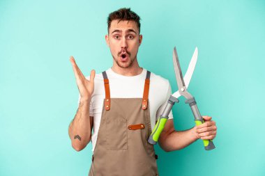 Genç bahçıvan beyaz bir adam mavi arka planda izole edilmiş bir makas tutuyor. Şaşırmış ve şok olmuş..