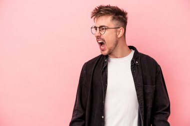 Pembe arka planda izole edilmiş genç beyaz adam çok kızgın, öfkeli, hayal kırıklığına uğramış diye bağırıyor..