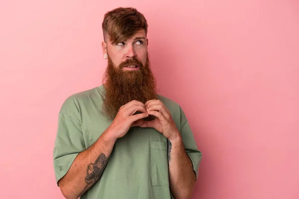 Young caucasian ginger man with long beard isolated on pink background making up plan in mind, setting up an idea.