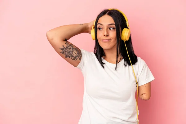 Young caucasian woman with one arm listening to music isolated on pink background touching back of head, thinking and making a choice.