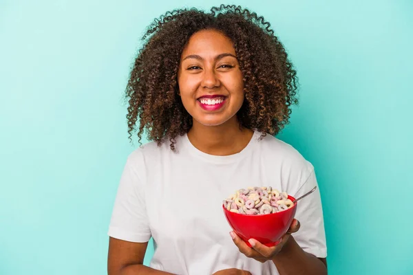 年轻的非洲裔美国女人拿着一碗谷物 被蓝色背景隔离 玩得很开心 — 图库照片