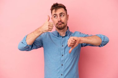 Pembe arka planda izole edilmiş genç beyaz bir adam baş parmağını kaldırıyor ve baş parmağıyla işaret ediyor. Zor bir seçim.