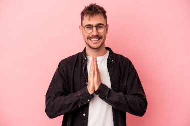 Pembe arka planda izole edilmiş genç beyaz bir adam. El ele tutuşup, ağız kenarında dua ediyor. Kendine güveniyor..