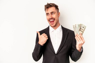 Kafkasyalı genç bir iş adamı elinde banknotlar tutarken beyaz arka planda, parmak uzakta, gülerek ve kaygısızca izole edilmiş..