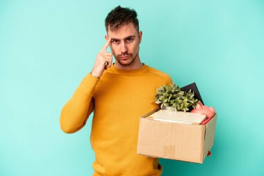 Kafkasyalı genç bir adam mavi arka planda izole edilmiş bir şekilde hareket ediyor. Şakağı işaret ediyor, düşünüyor, bir göreve odaklanıyor..