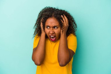 Mavi arka planda yalıtılmış kıvırcık saçlı, elleri kulaklarıyla yüksek ses duymamaya çalışan Afro-Amerikalı genç bir kadın..