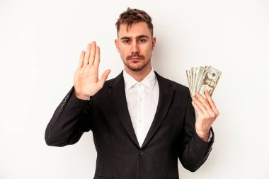 Beyaz arka planda izole edilmiş banknotlar tutan Kafkasyalı genç bir iş adamı elini uzatıp dur işareti göstererek seni engelliyor..